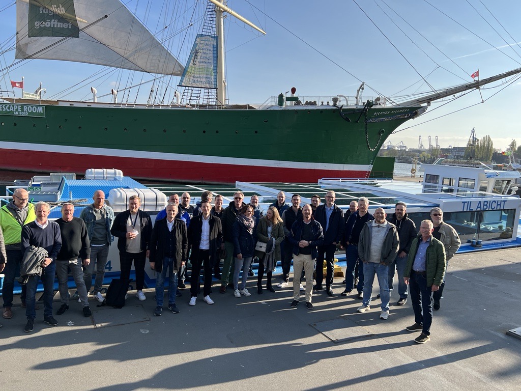 Gruppe posiert vor historischem Segelschiff im Hafenbereich